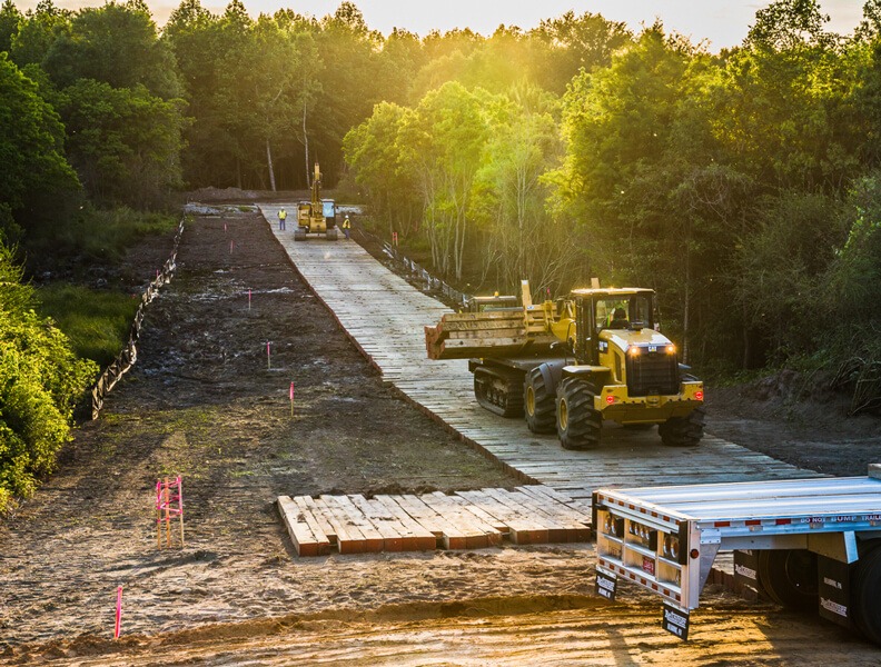 Wooden access mats over mud between trees.